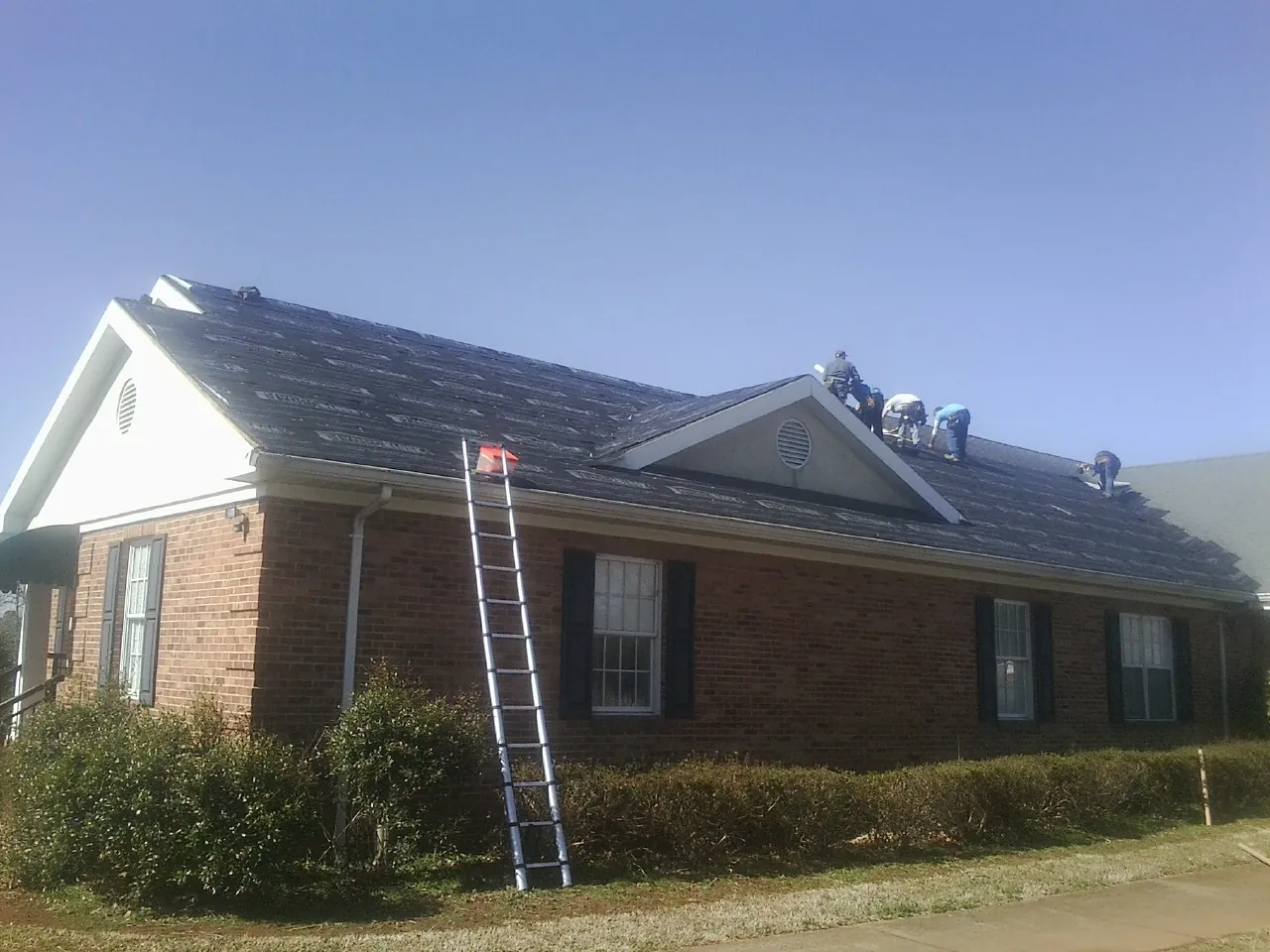 Crew tearing shingles off a brick ranch roof with a ladder set — Emergency Roof Repair work by our crew in Joliet
