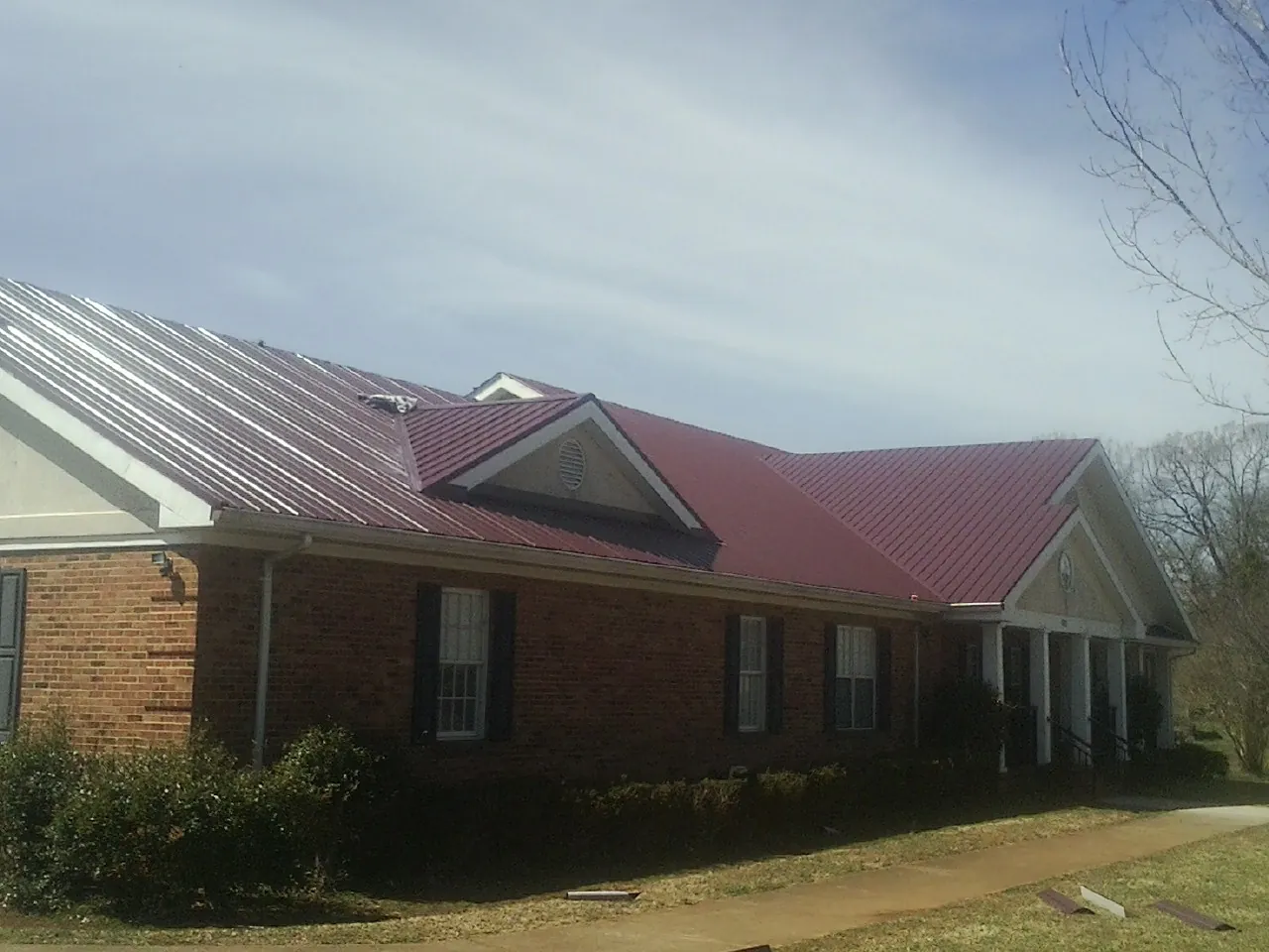 Red metal roof with gabled entries on a long brick building, from a Hail Damage Roof Repair job in Joliet