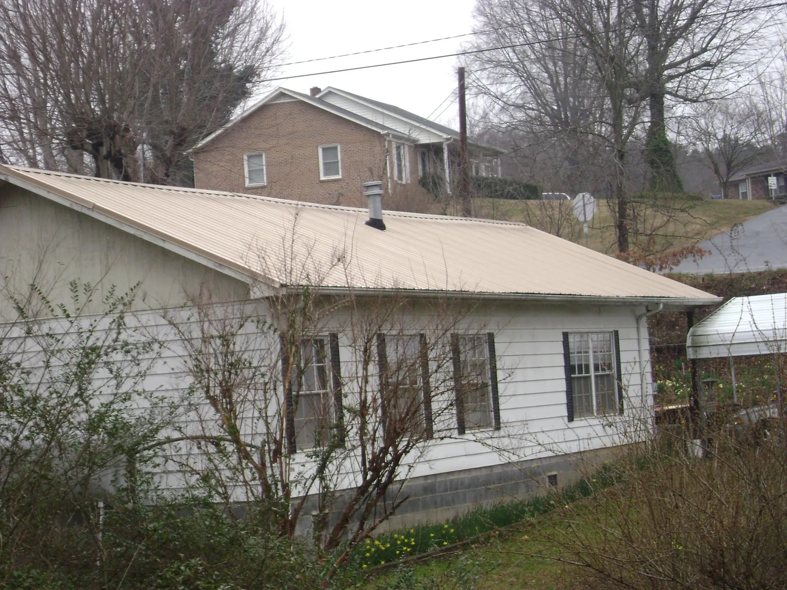 Tan metal roof on a white sided house set into a hillside — Commercial Roofing by Roofing Brothers in Joliet