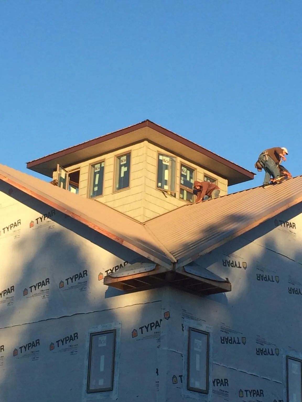 Roofers working around a rooftop cupola on a new metal roof at sunset — Roof Waterproofing in Joliet by Roofing Brothers